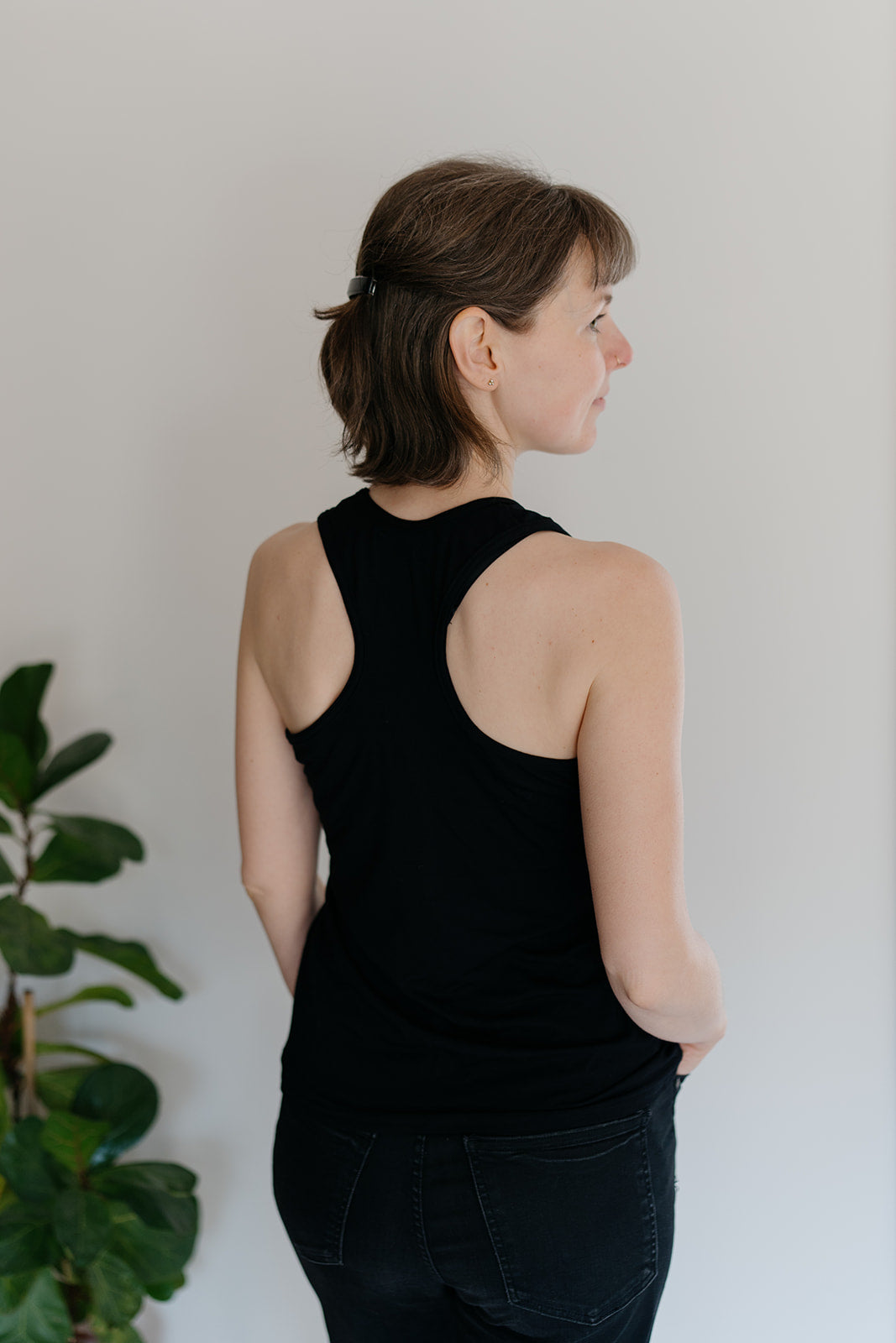 A woman viewed from behind wearing a black racerback tank top, with a plant in the background
