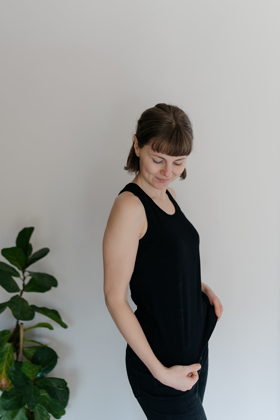 A woman viewed from the side wearing a black racerback tank top, with a plant in the background