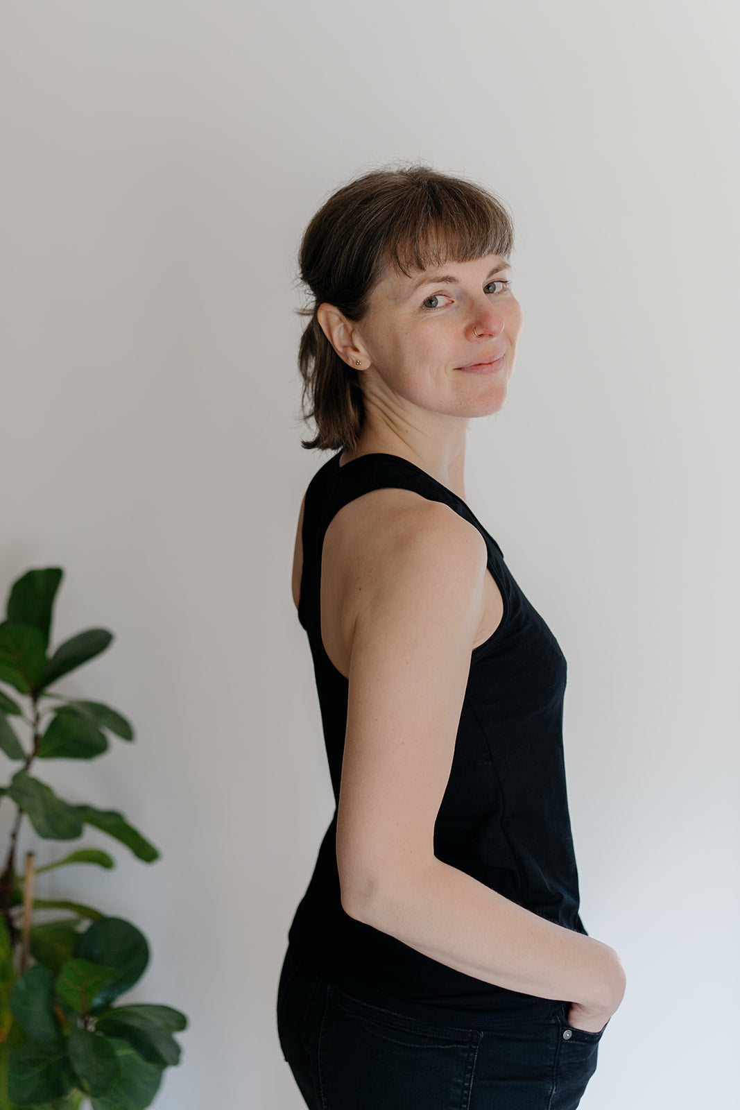 A woman viewed from the side wearing a black racerback tank top, with a plant in the background