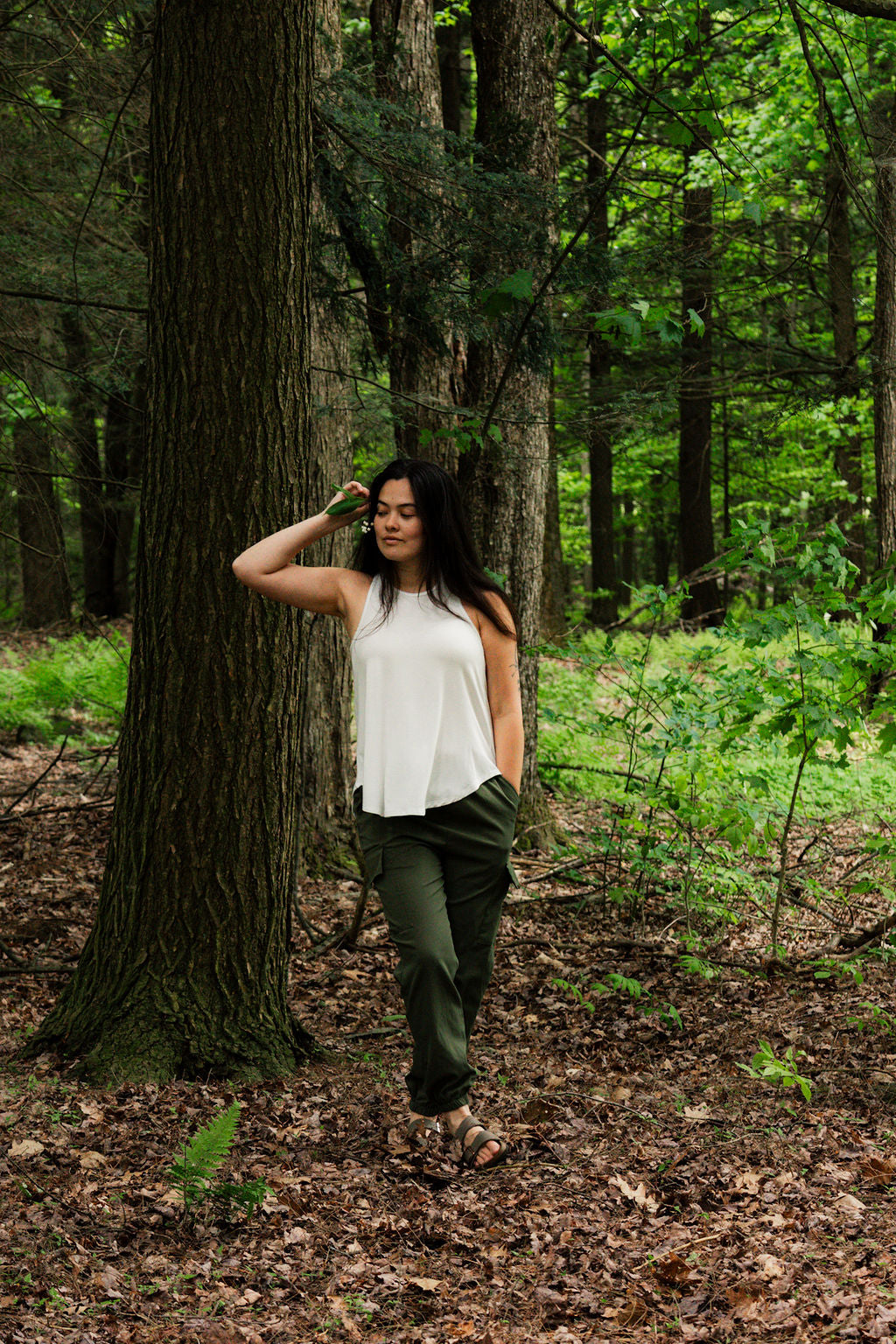 Woman standing in a forest with trees and greenery around her