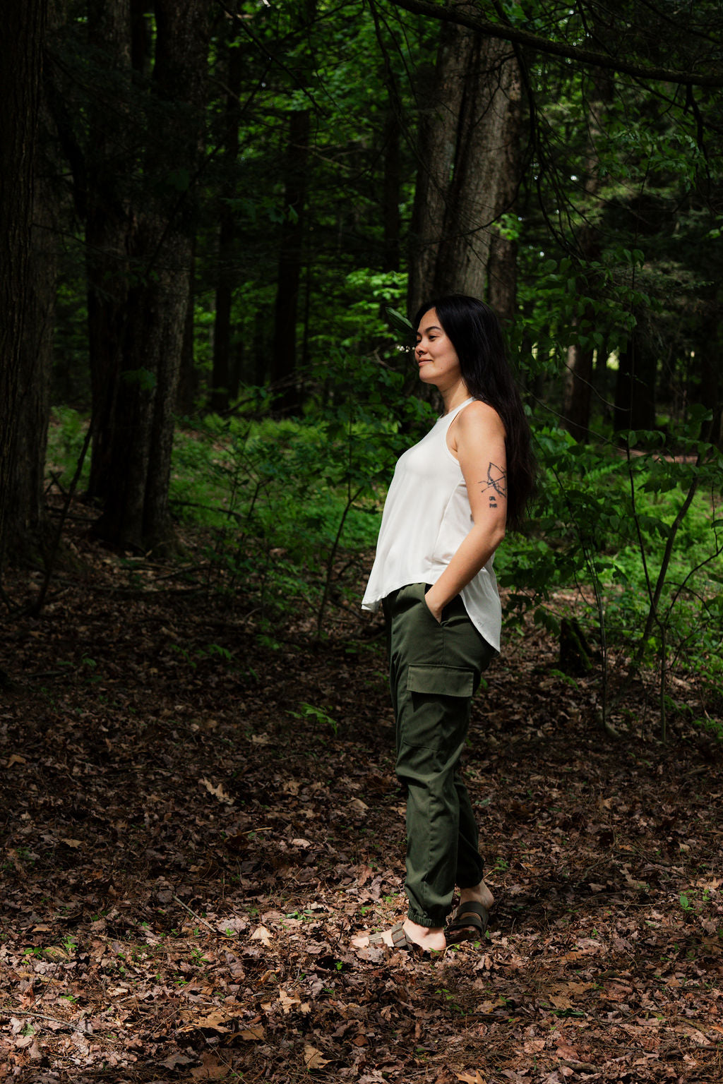 Woman in a white top and green pants standing in a forest