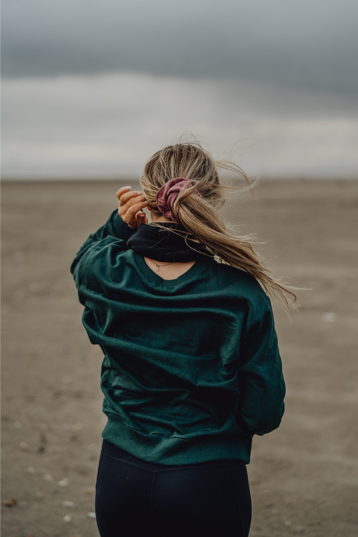A person standing with their back towards the camera, wearing a pink French terry scrunchie in their hair, with the beach in the background.