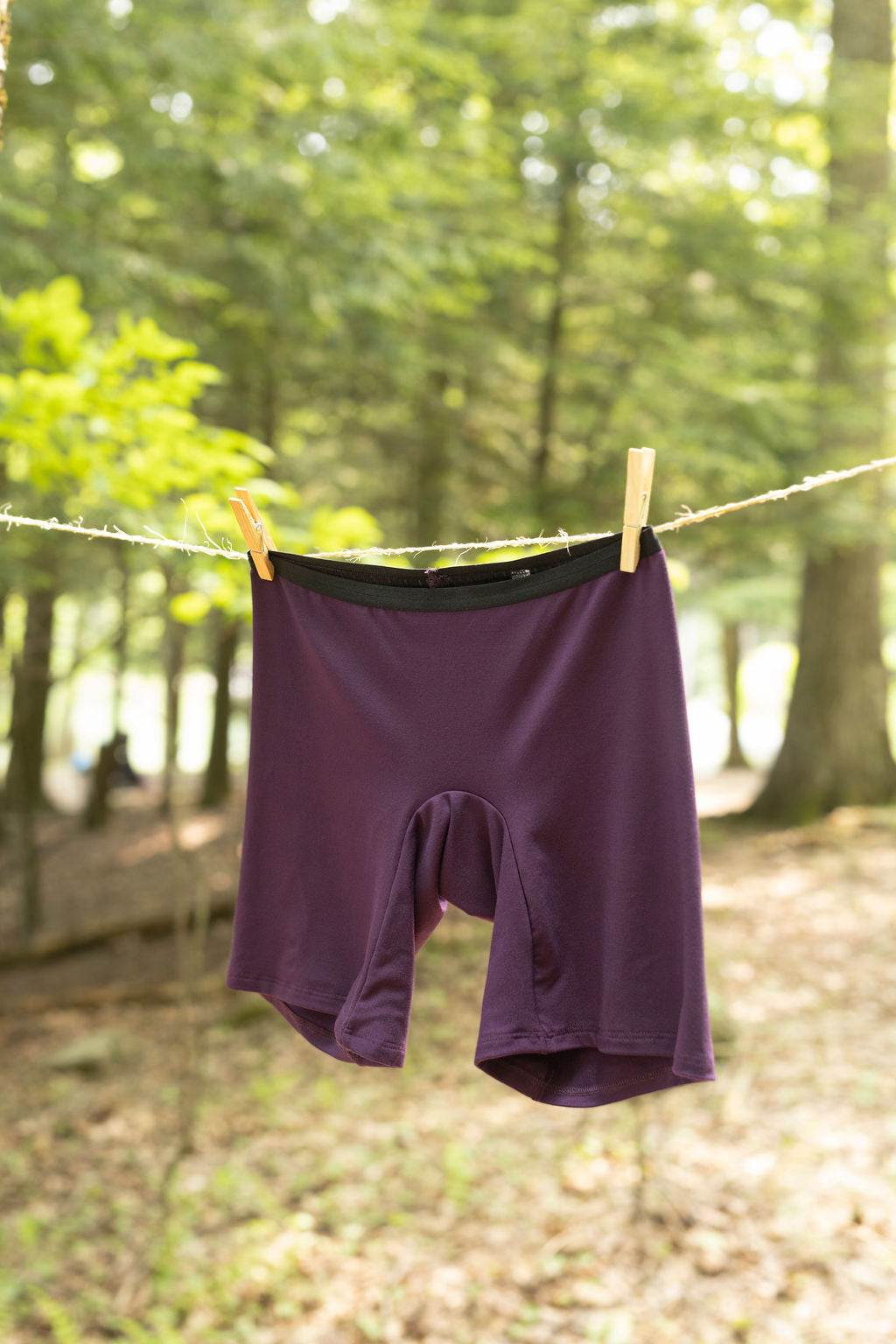 Purple women's bamboo underwear hanging on a clothesline in a forest setting