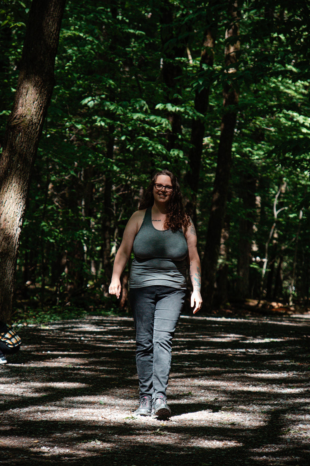 Person walking on a path in a forest wearing a grey tank top