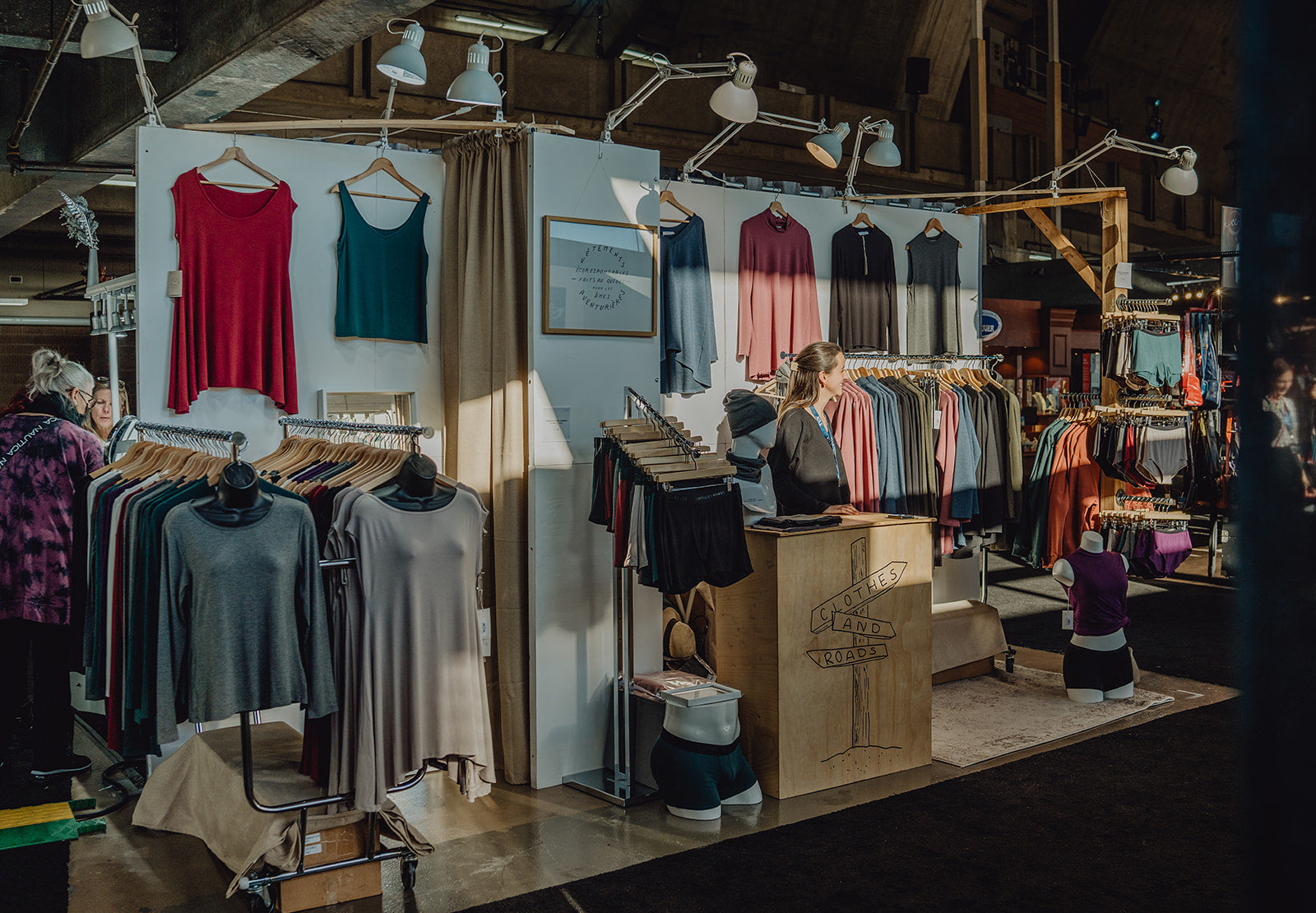 Clothes & Roads booth at an event, showcasing minimalist and eco-conscious clothing, with the designer behind the counter.