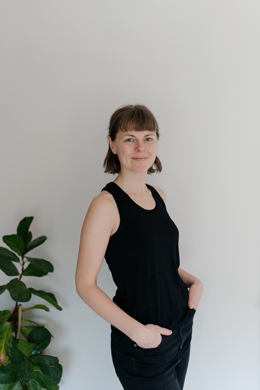 A woman viewed from the side wearing a black racerback tank top, with a plant in the background