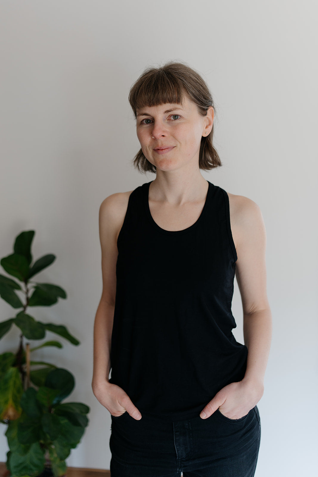 A woman wearing a black racerback tank top, with a plant in the background