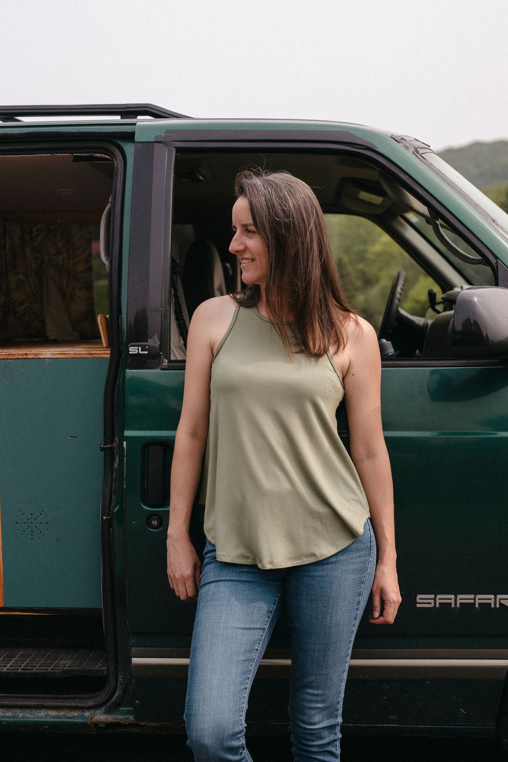 Woman wearing a sage tank top standing next to a green vehicle with open door