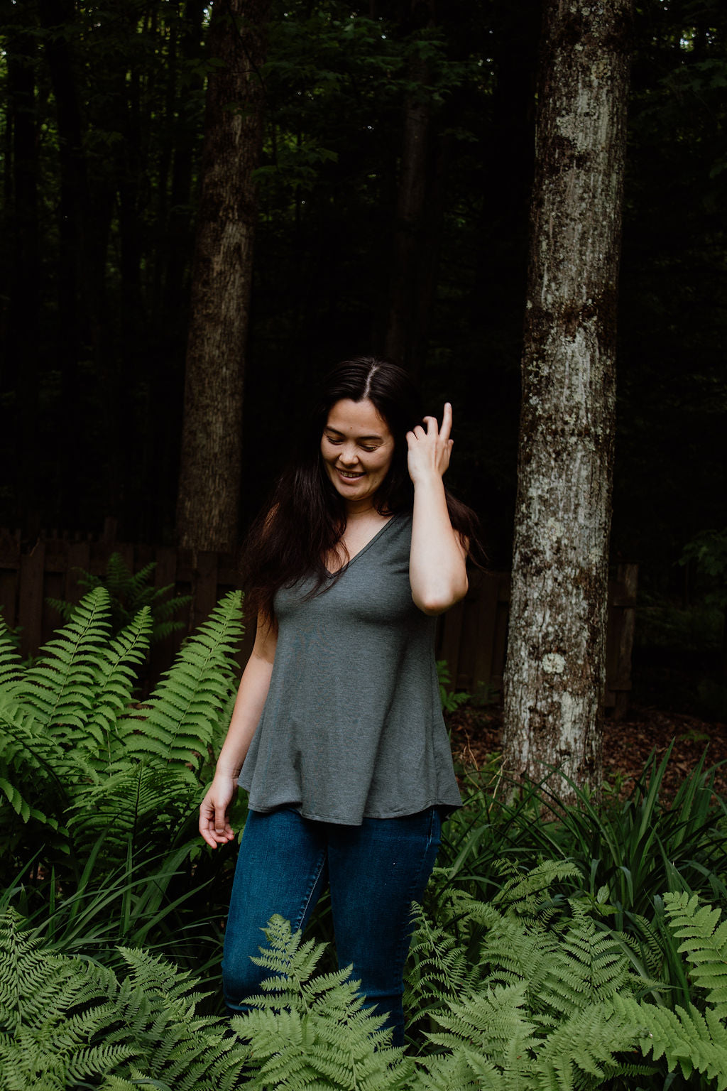 Woman standing among ferns in a forest wearing a gray V-neck camisole