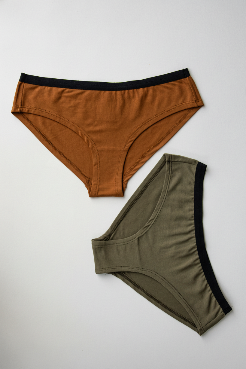 Two pairs of bikini women's underwear, one orange and one green, on a light gray background.