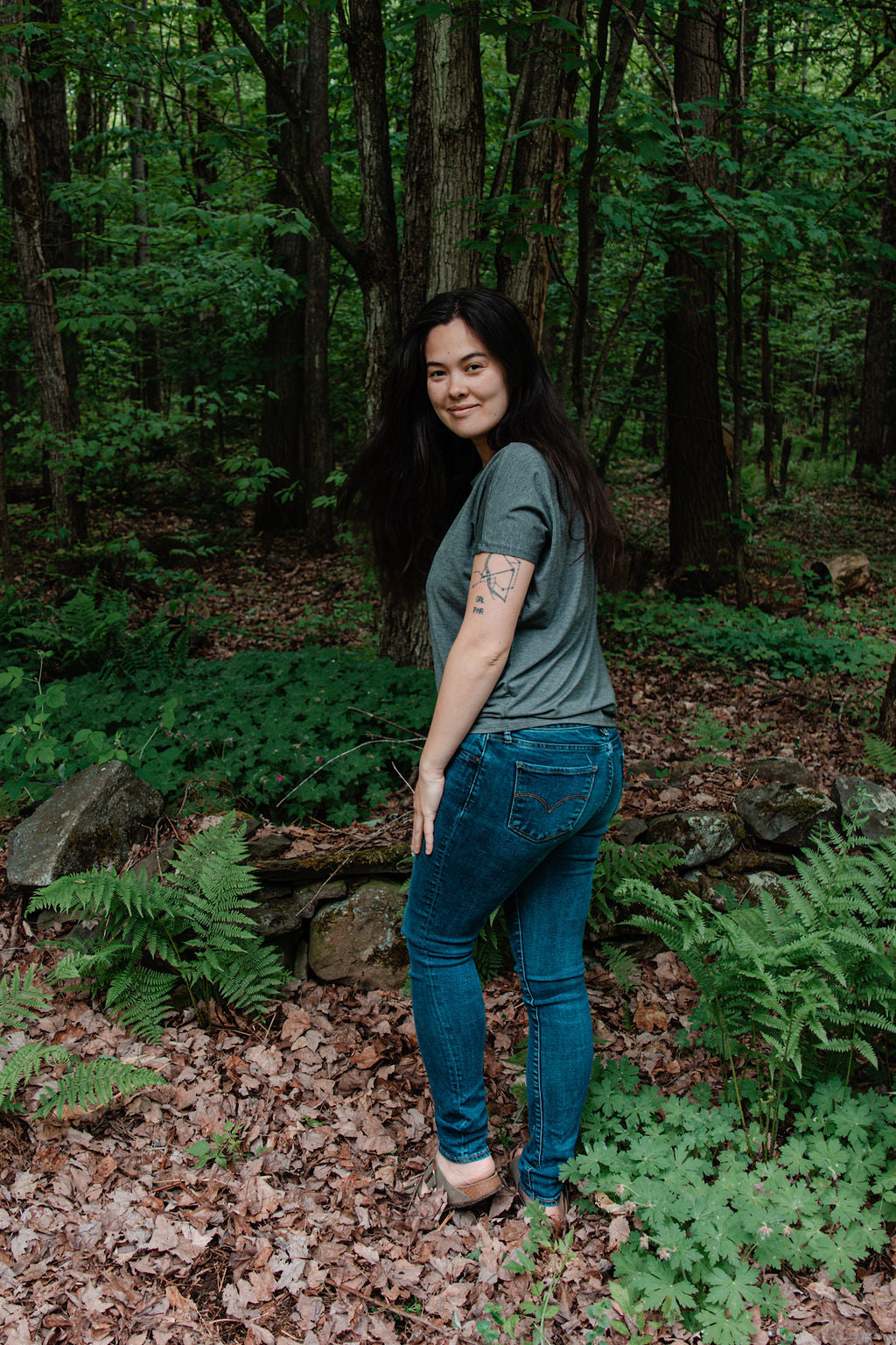 Woman standing in a forest with greenery and trees around her.