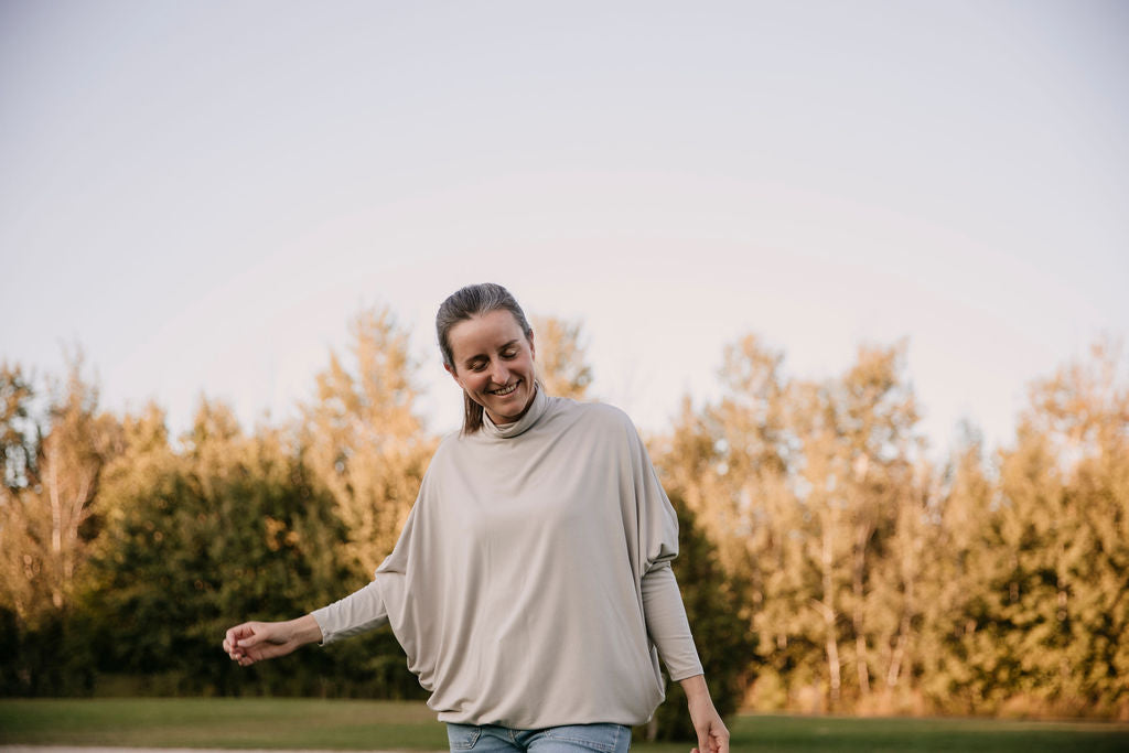 Woman wearing The Batwing Long-Sleeve Top in Taupe, standing outdoors with trees in the background.