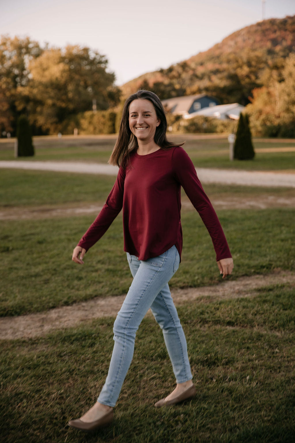 Woman wearing The Breezy Long-Sleeve Shirt in Porto, walking in a field with a mountain in the background.
