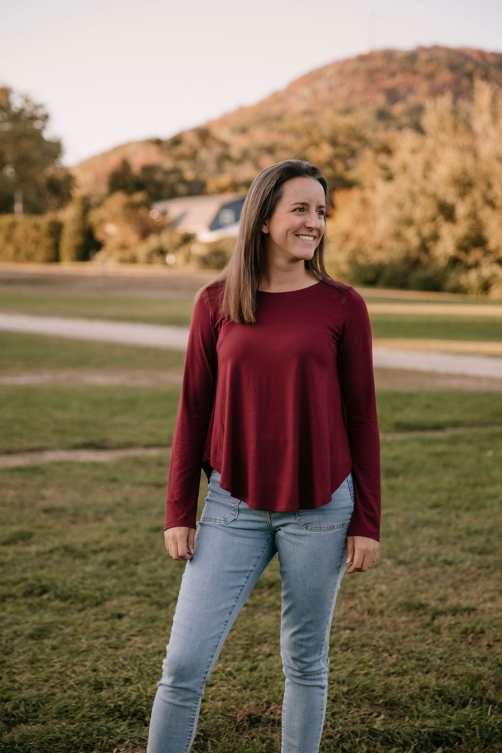 Woman wearing The Breezy Long-Sleeve Shirt in Porto, standing in a field with a mountain in the background.