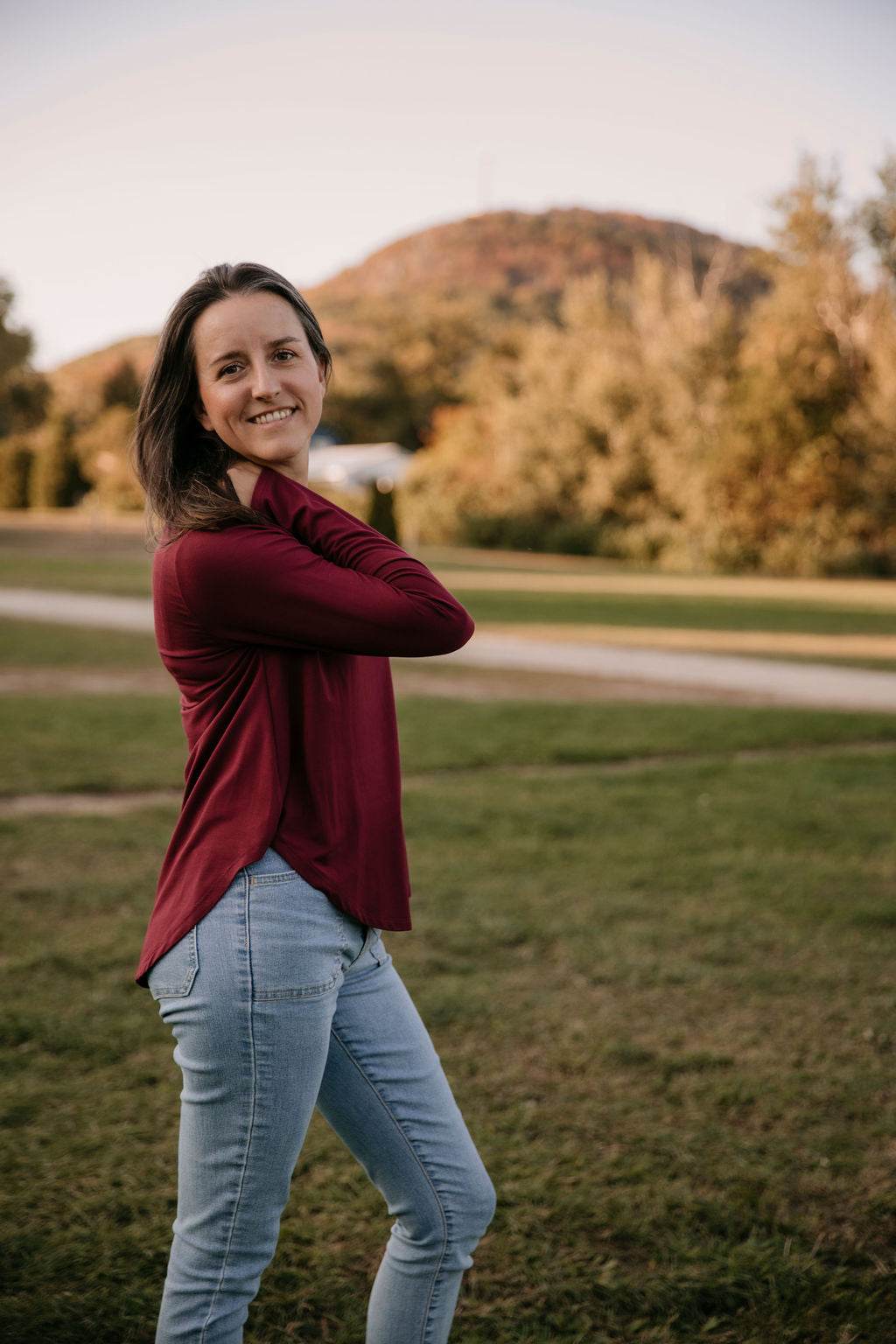Woman wearing The Breezy Long-Sleeve Shirt in Porto, standing in a field with a mountain in the background.