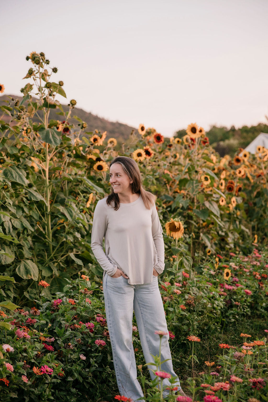 Woman wearing The Breezy Long-Sleeve Shirt in Taupe, standing in a field of sunflowers and other flowers.