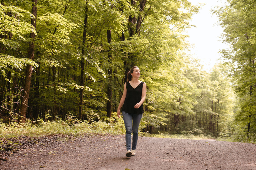 Woman wearing a black v-neck tank top walking on a path through a forest
