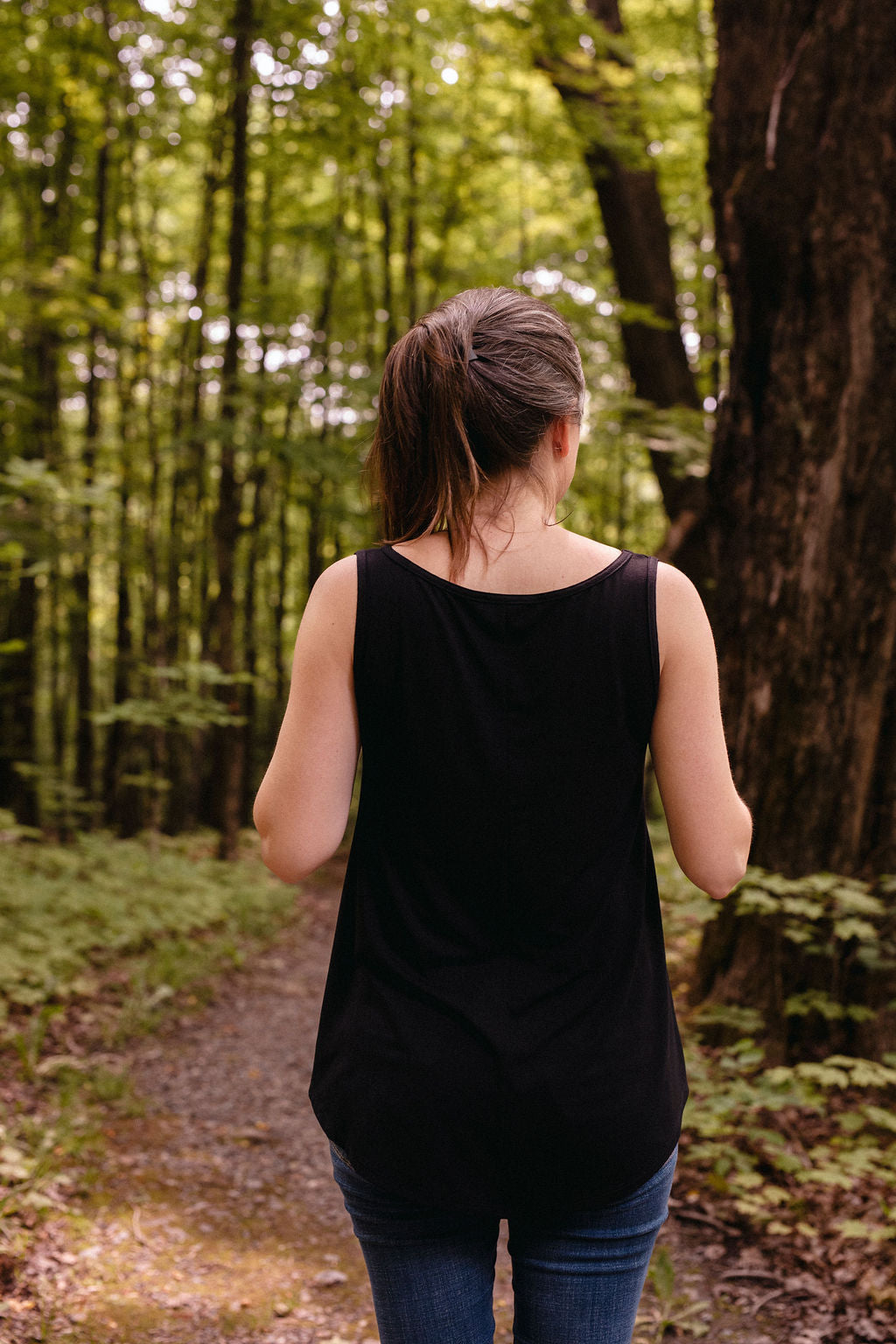 Woman wearing a black tank top walking away from the camera on a forest path
