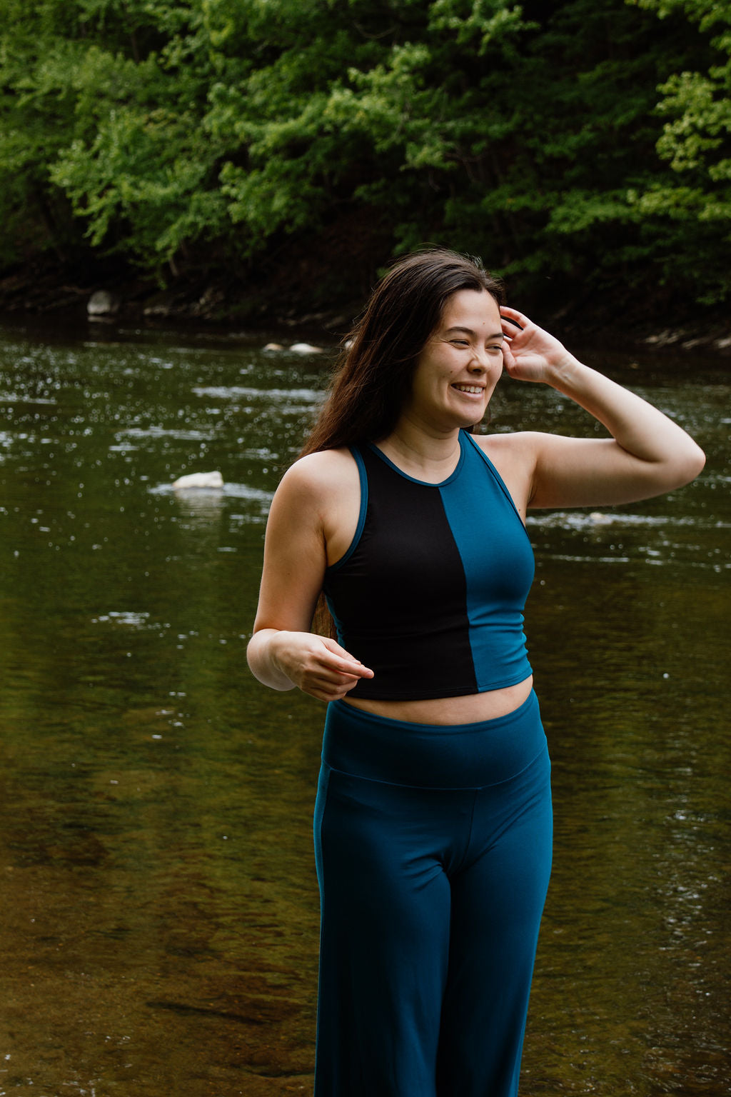 Women in tealand black crop top and teal palazzo pants in front of a river