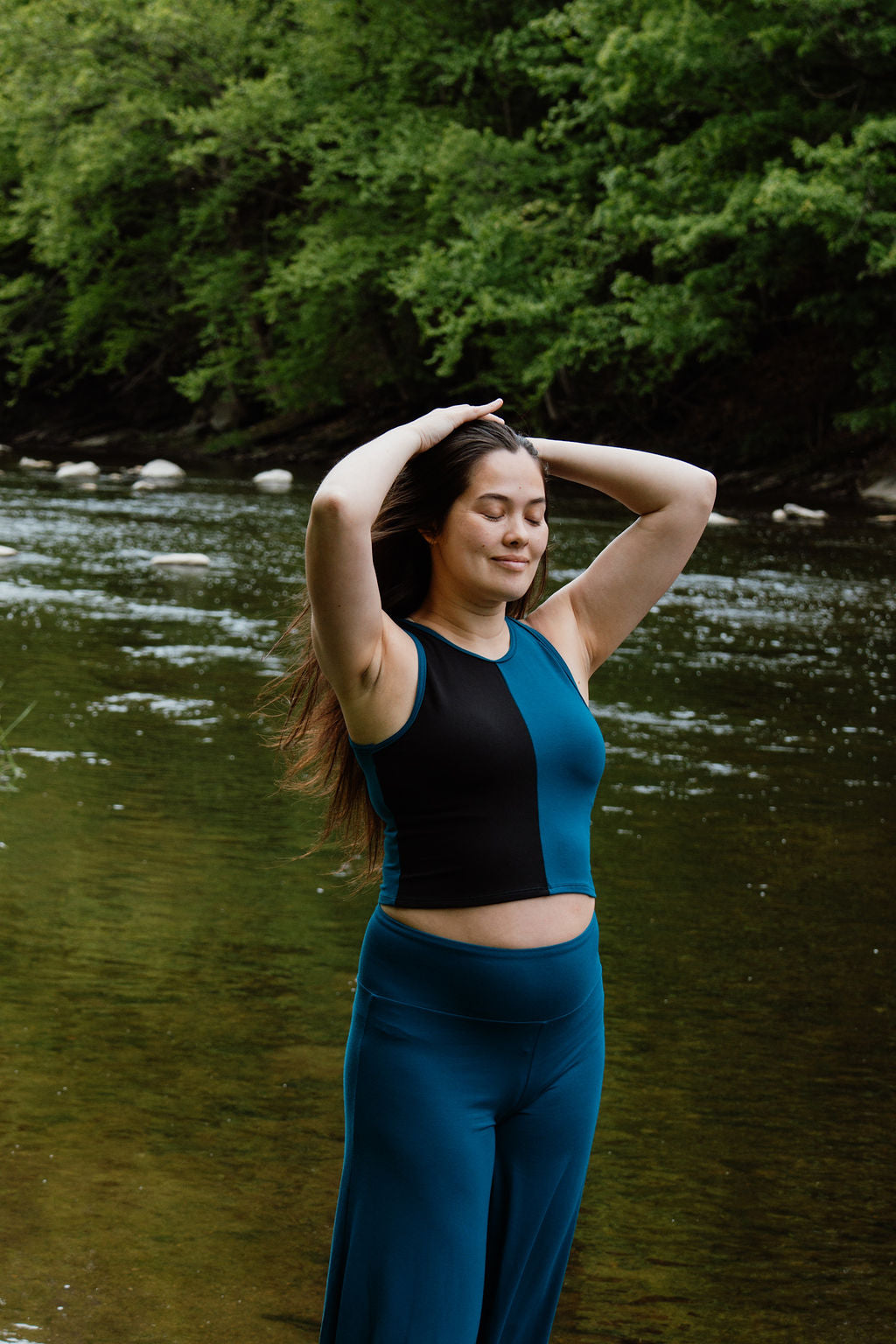 Women in tealand black crop top and teal palazzo pants in front of a river