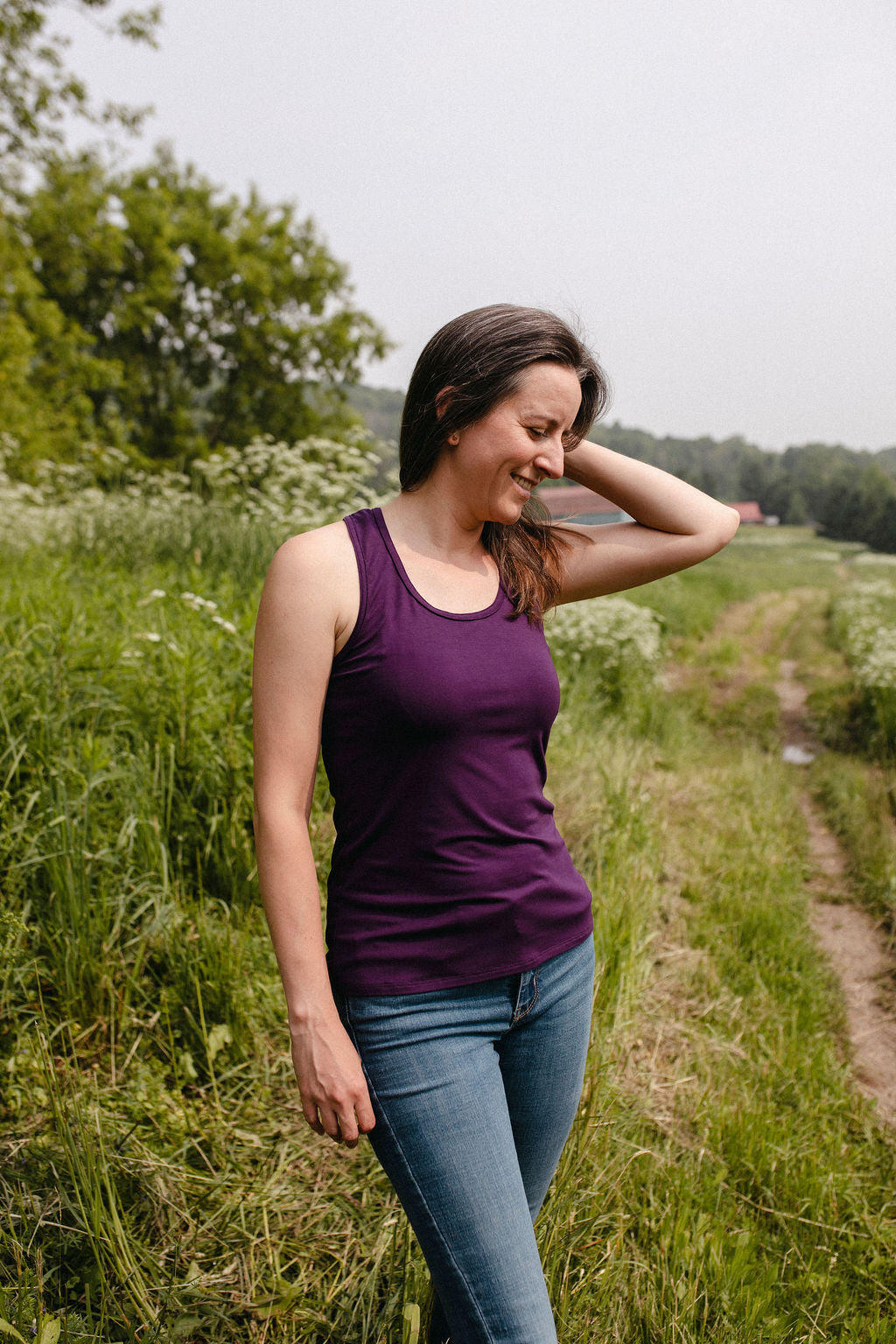 Woman in a purple tank top standing in a grassy field with trees in the background