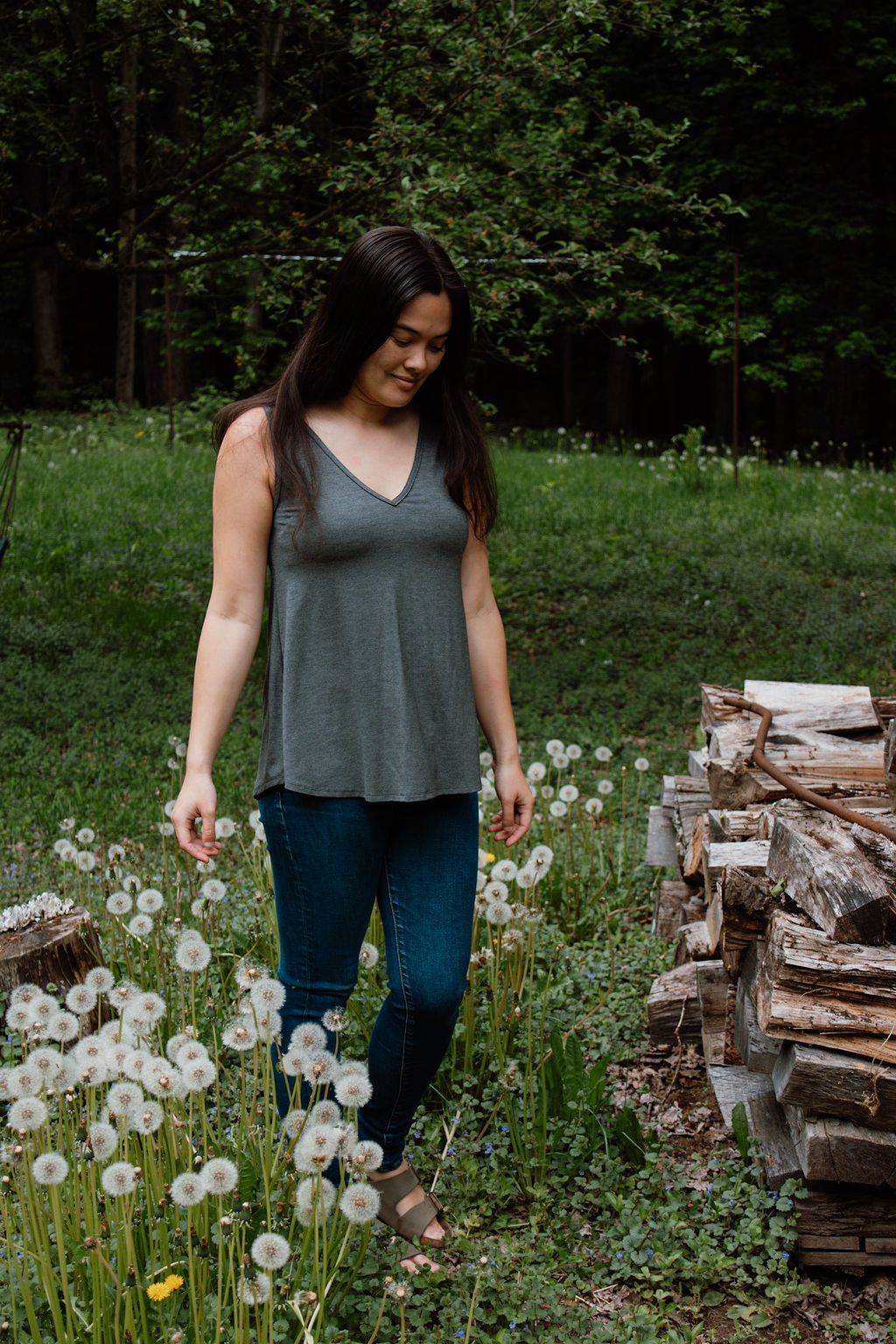 Woman walking through a field of dandelions with a stack of firewood in the background