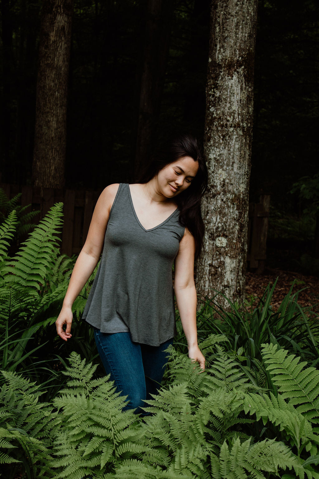 Woman standing among ferns in a forest wearing a gray V-neck camisole