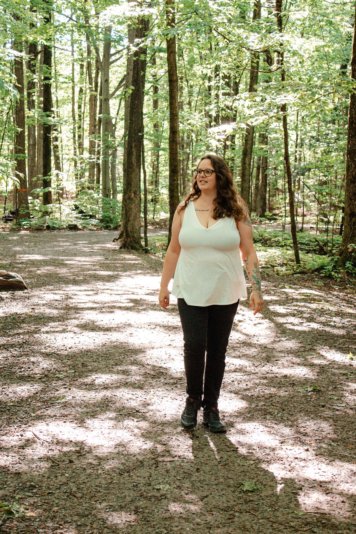 Woman standing in a forest with sunlight filtering through trees wearing an ivory V-neck camisole