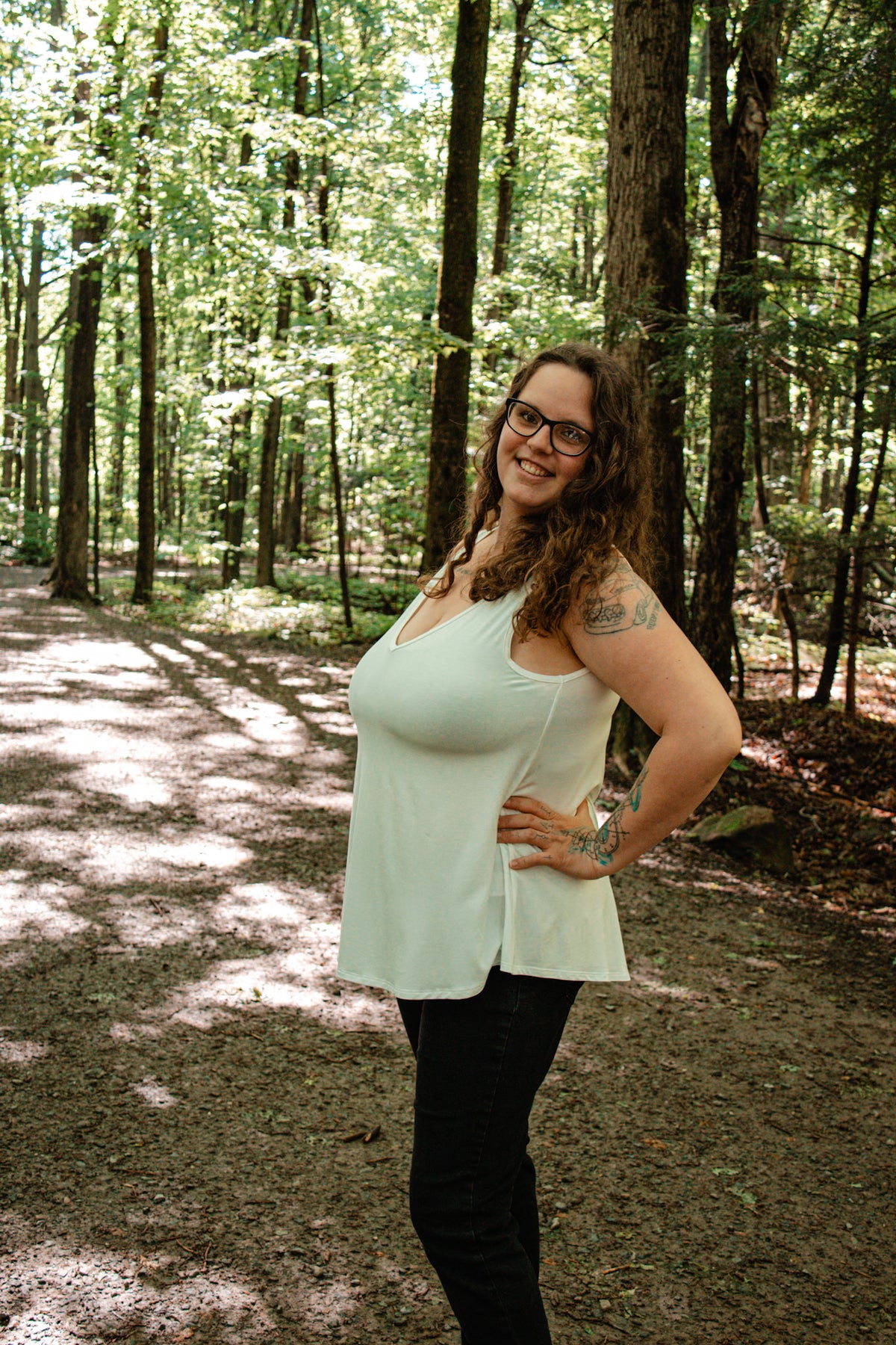 Woman standing in a forest with sunlight filtering through trees wearing an ivory V-neck camisole