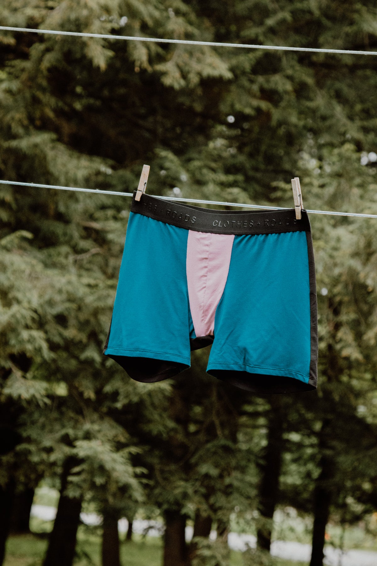 Close-up of men’s boxer briefs hanging on a clothesline with trees in the background.