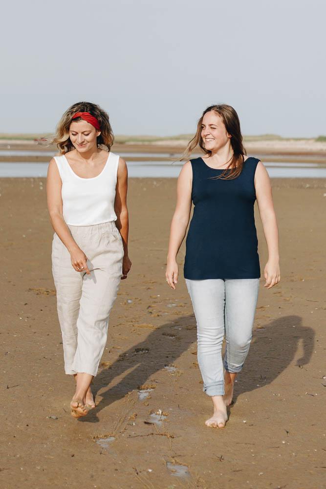 Two women on the beach wearing the ivory and navy blue reversible bamboo camisole, front view.